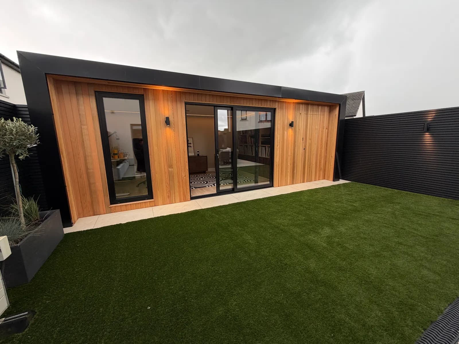 Cedar clad garden room at dusk with outdoor lighting and artificial lawn