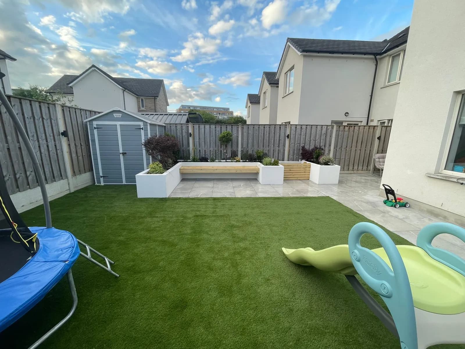 Family garden with artificial grass, trampoline and raised planter seating