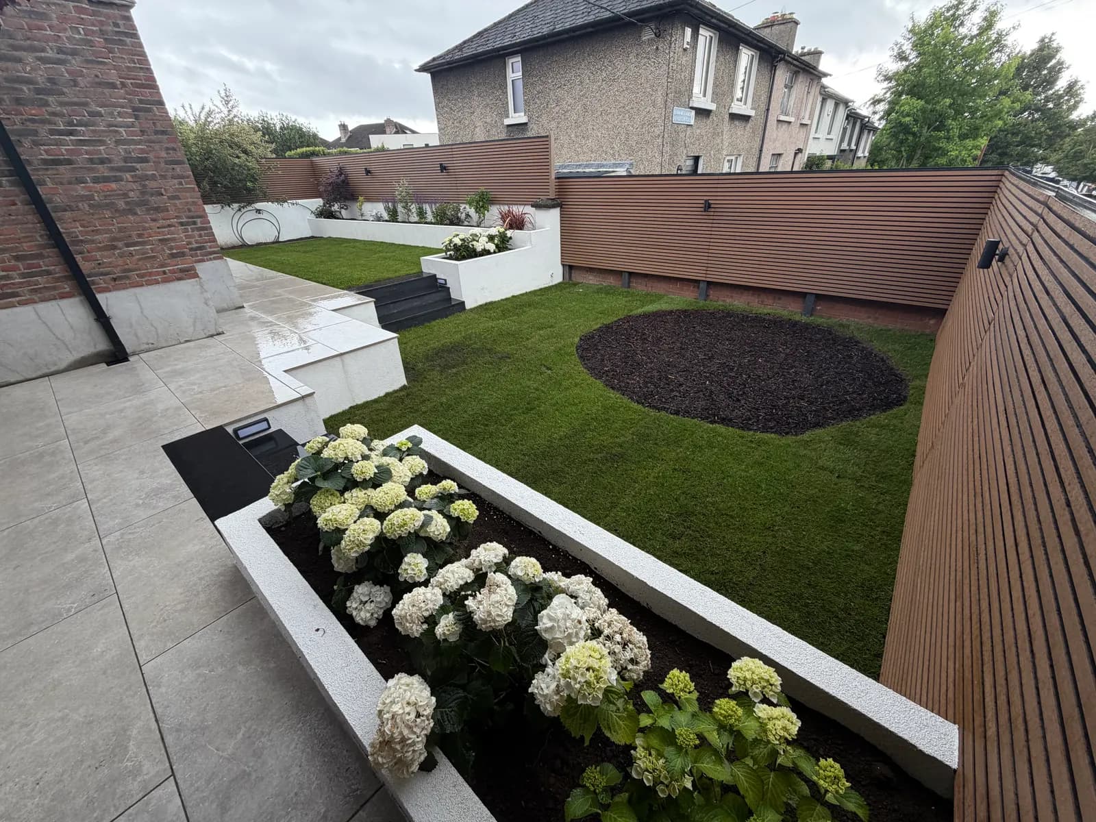 Natural lawn with white raised beds, hydrangeas and composite fencing
