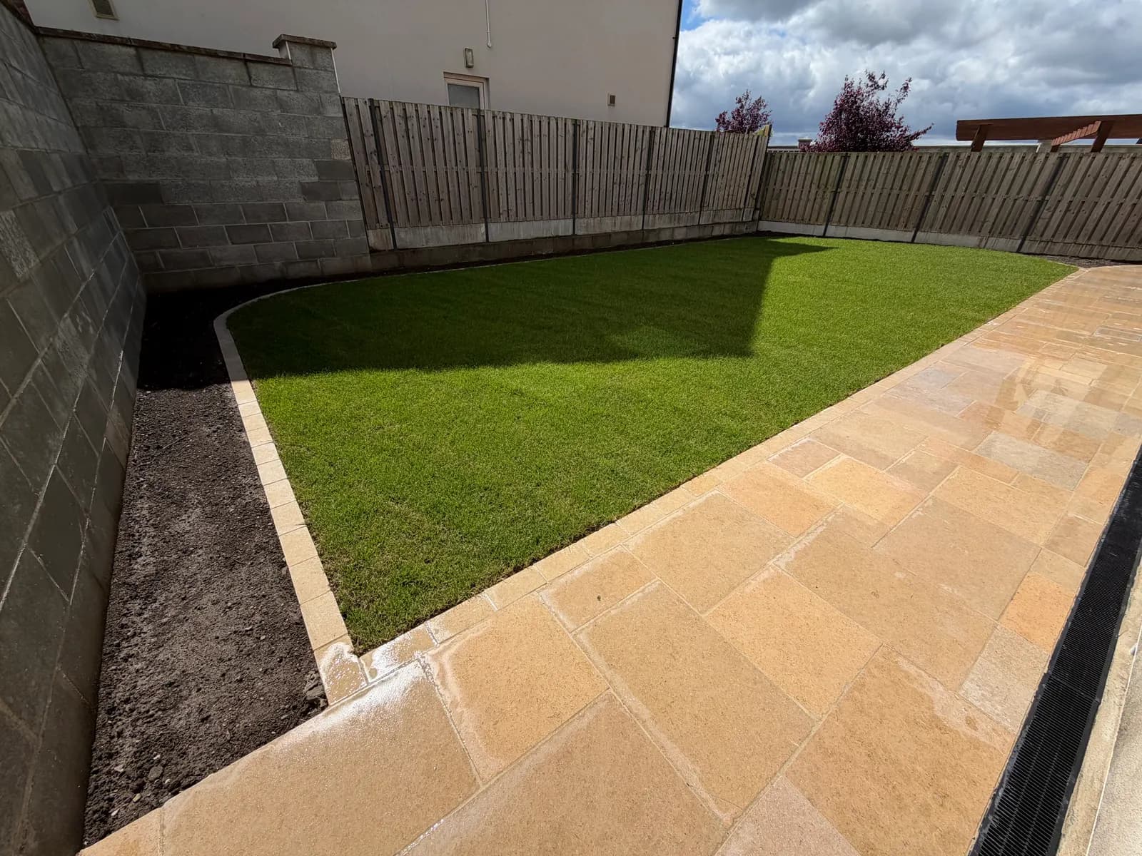 Newly laid turf lawn with curved sandstone paving edge